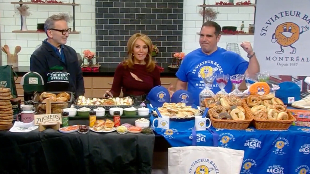 Matt Pomerance from Zucker's Bagels stands on one side of a table covered in bagels and merch, while Vince Morena of St-Viateur Bagel pumps a fist.