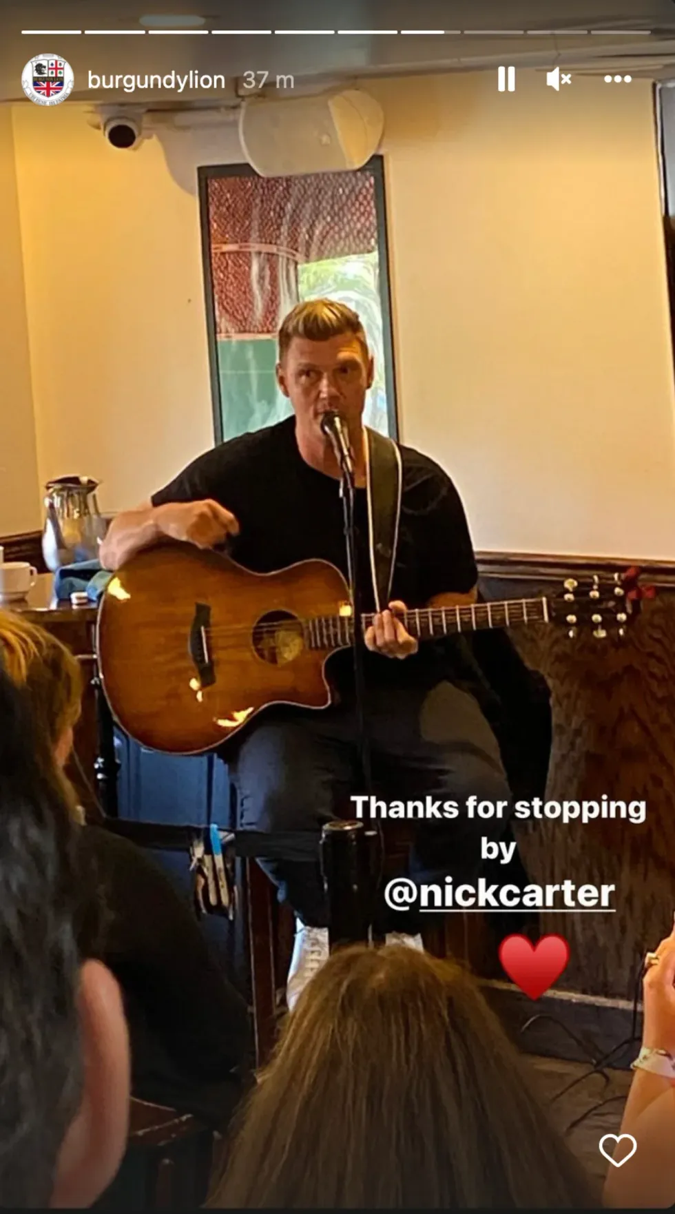 Nick Carter performing at a Montreal restaurant playing the guitar while sitting on a stool.