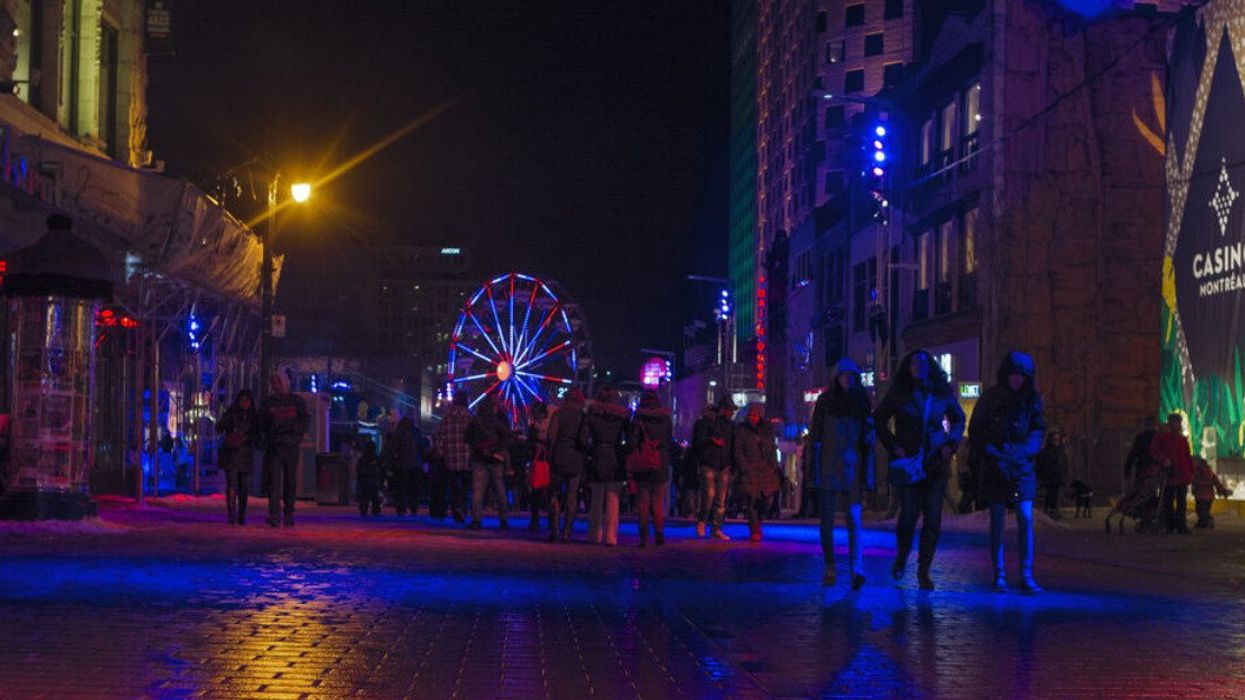 Night scene at Montreal en Lumiere. A view of people walking on Ste-Catherine street with an illuminated big wheel in the background.