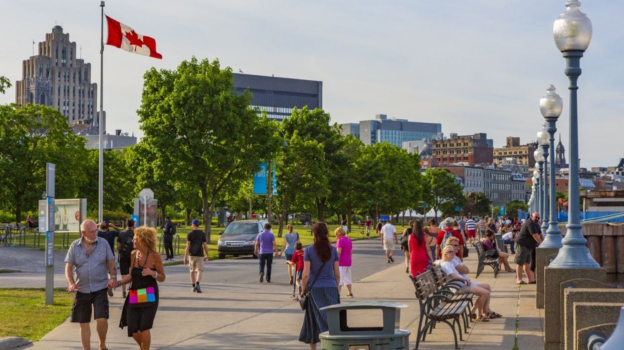 Older people walking the promenade at the Old Port in Montreal the downtown skyline in the background and a Canadian flag waving.