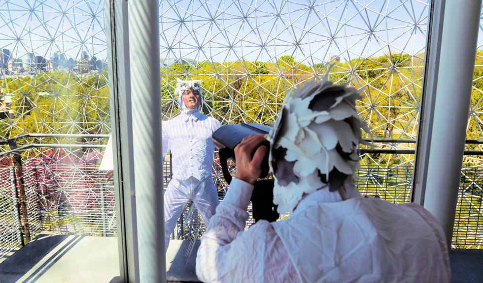 One performer in a bird costume uses the Biosphere binoculars to look at another bird performer.
