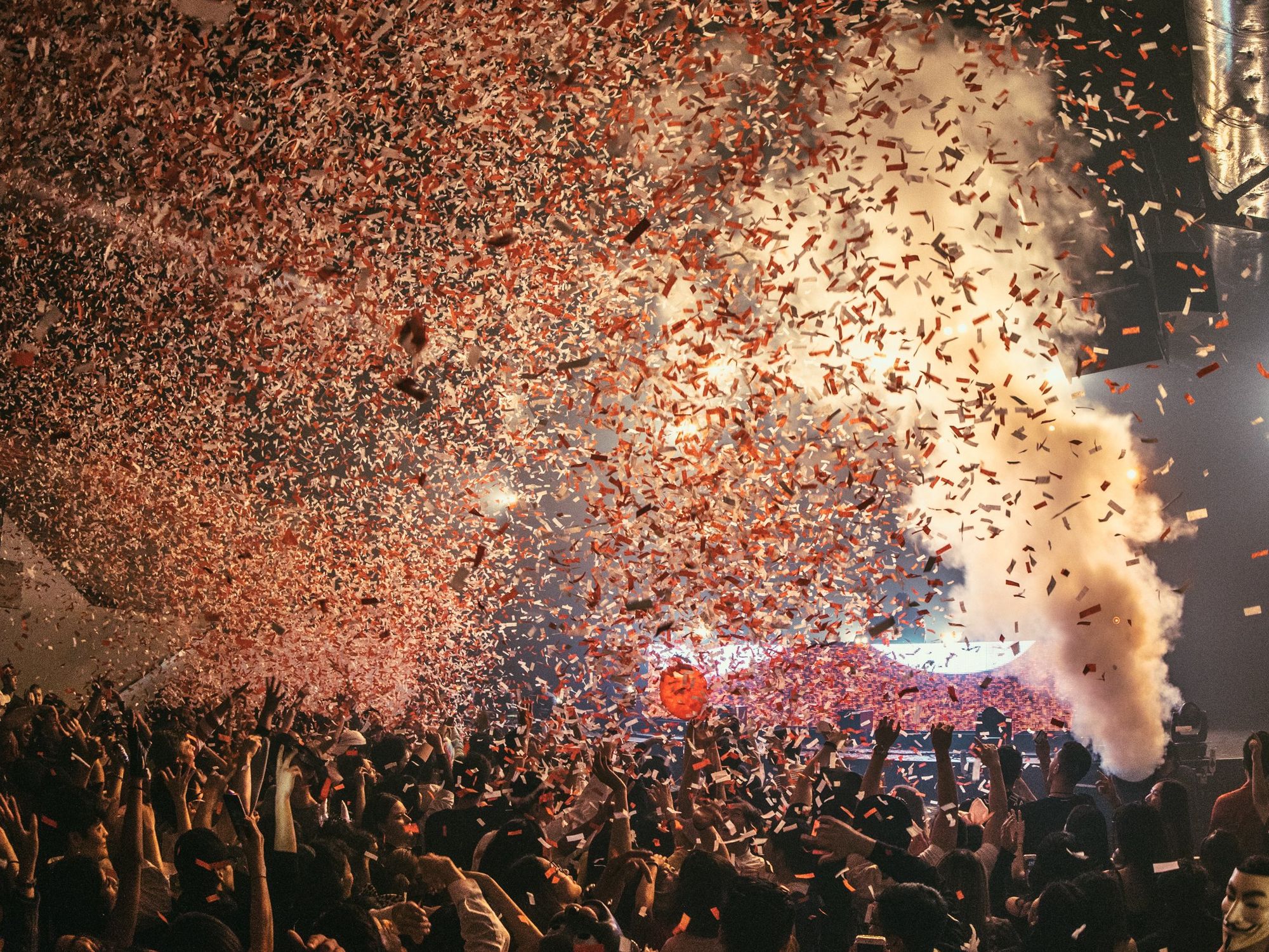 Orange, black and white ticker tape falls onto a crowd in front of the stage.