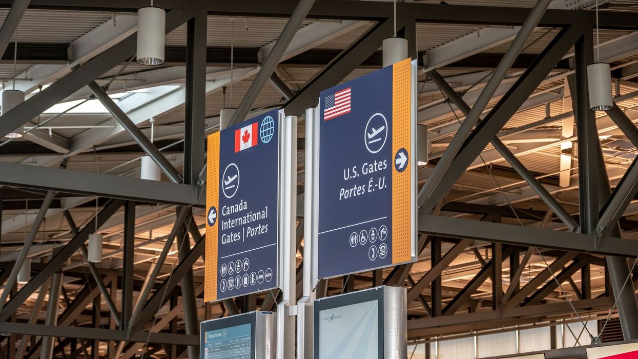 Overhead airport signage directing travellers to Canada international gates on the left and U.S. gates on the right.