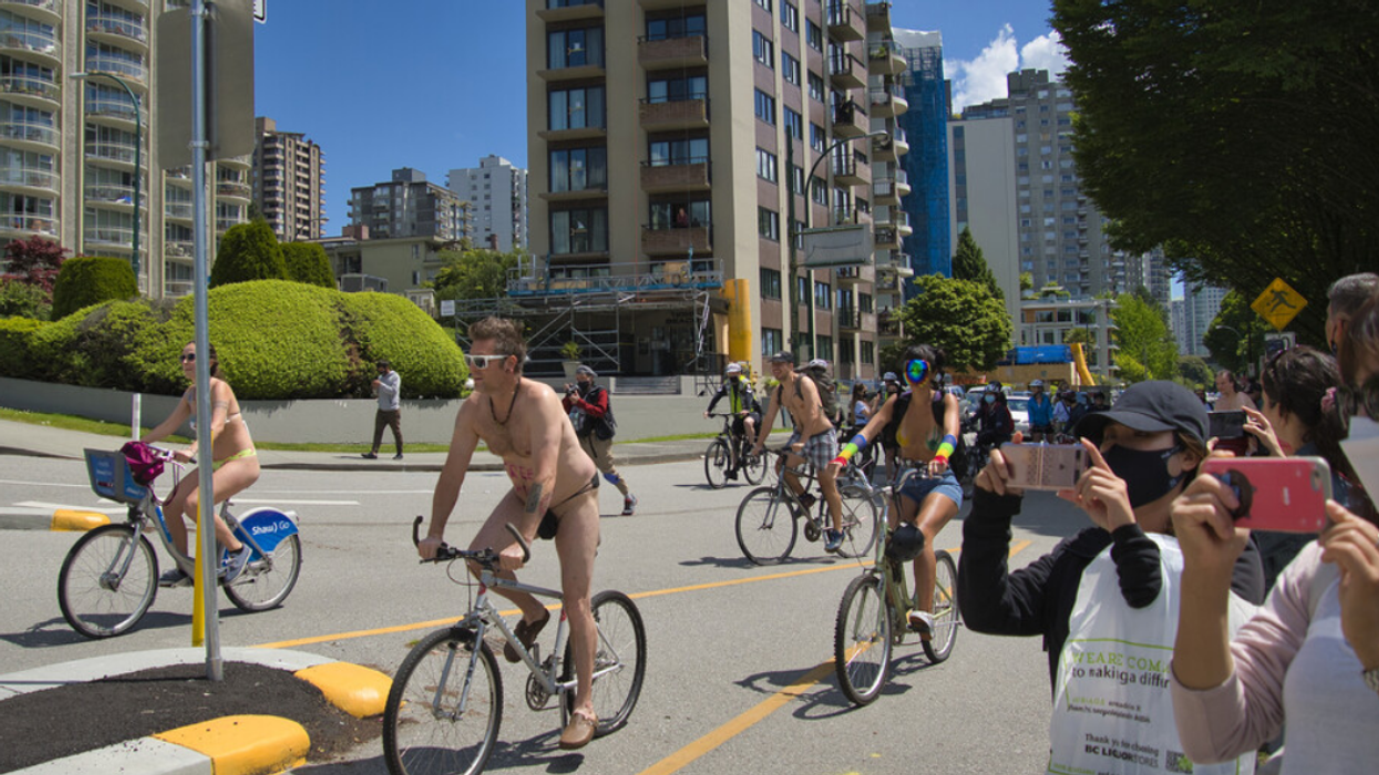 People bike through Vancouver streets in minimal clothing as onlookers snap photos.