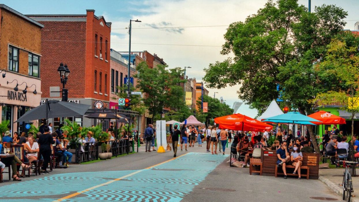 People gather under umbrellas, near trees, on rue Mont Royal during the summer.