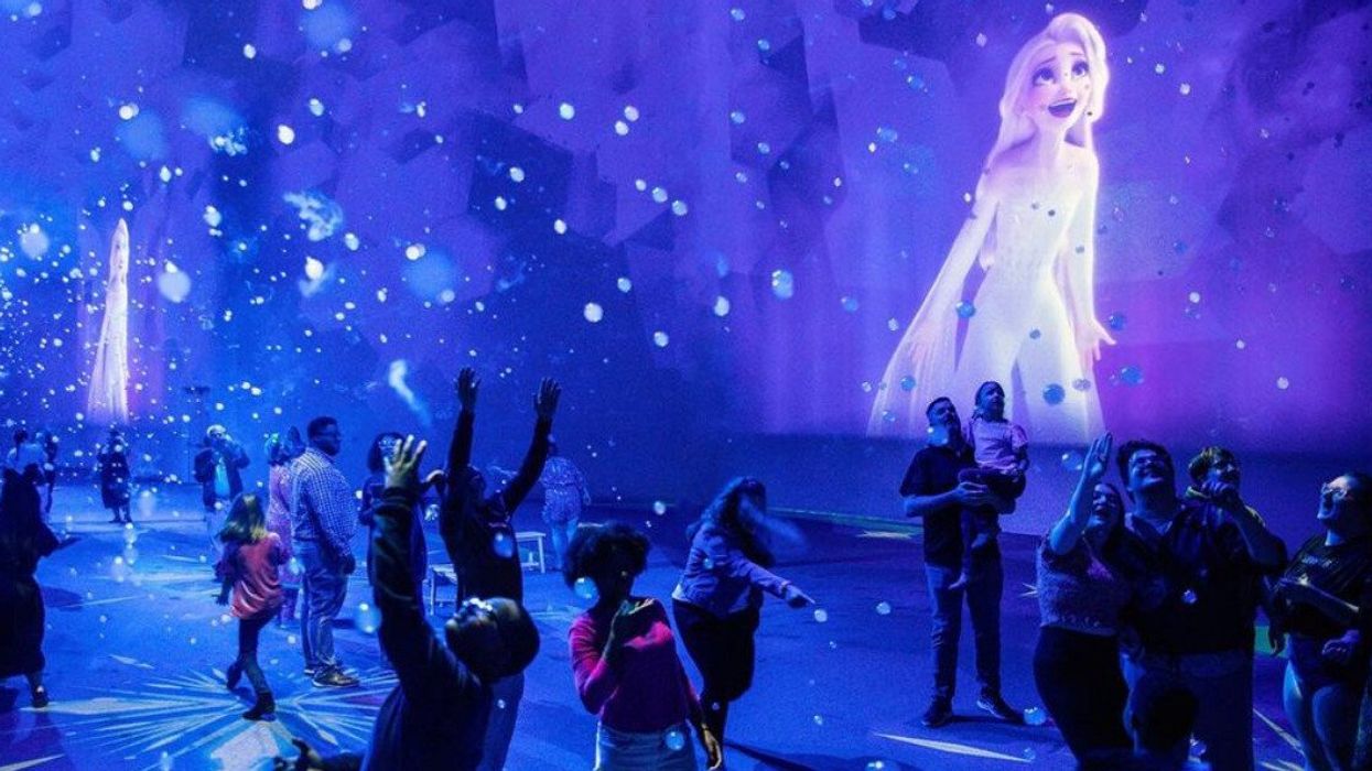 People in a room surrounded by purple and blue projections from the Disney film 'Frozen.'