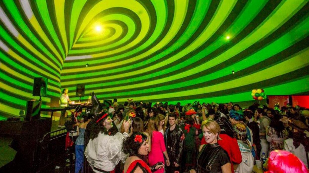 People in costumes dance in front of a DJ and under a striped neon green dome.