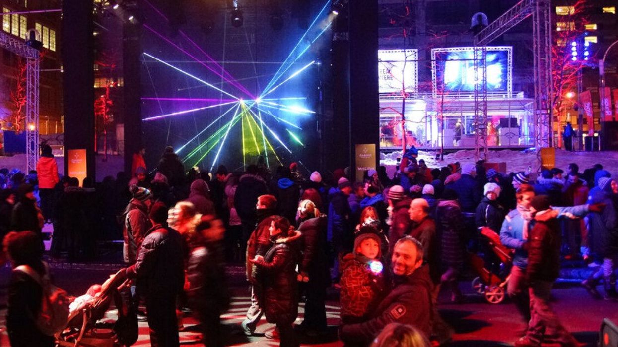 People in downtown Montreal at night during the winter, with a Montréal en Lumière installation in the background.