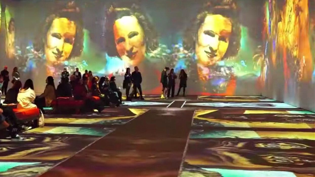 People sit in a room with floor-to-ceiling projects of Salvador Dalí's artwork.