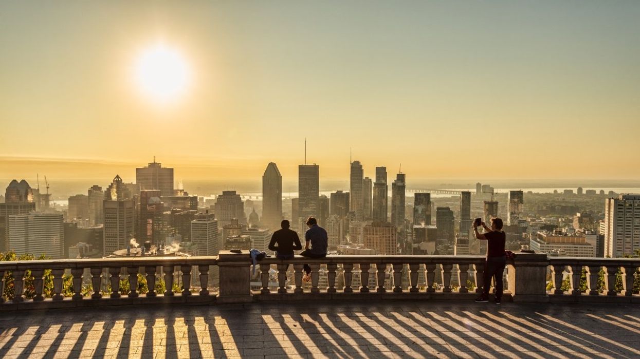 People sitting at the Mont-Royal lookout during the summer with views of the Montreal skyline and the sun.