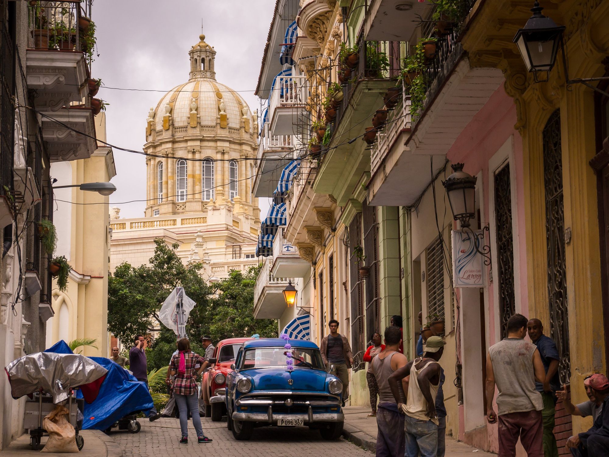 People stand around old cars in a street overlooking the capitol building in Havana.