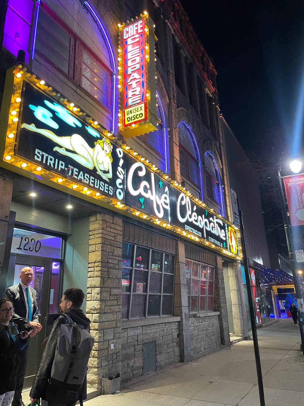 People stand in front of Cafe Cleopatra, located in Montreal's Quartier des spectacles, during the evening.