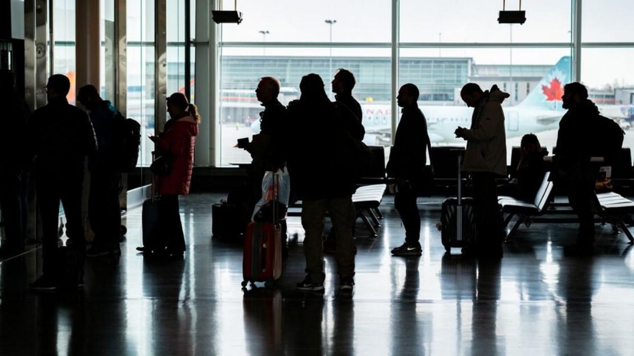 People stand in line at the passport check-in for a flight at Montreal's Trudeau airport with an Air Canada plane in the background.