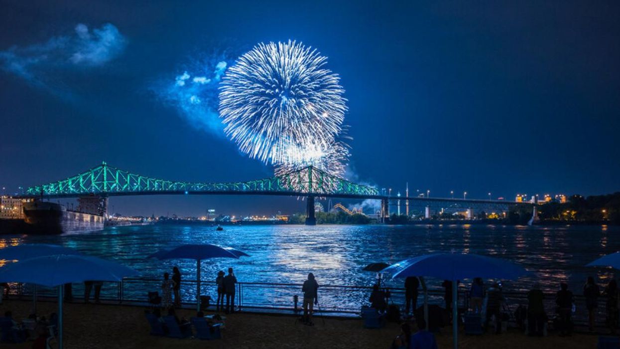 People stand on the Clock Tower Beach watching the fireworks show over the Jacques Cartier Bridge.