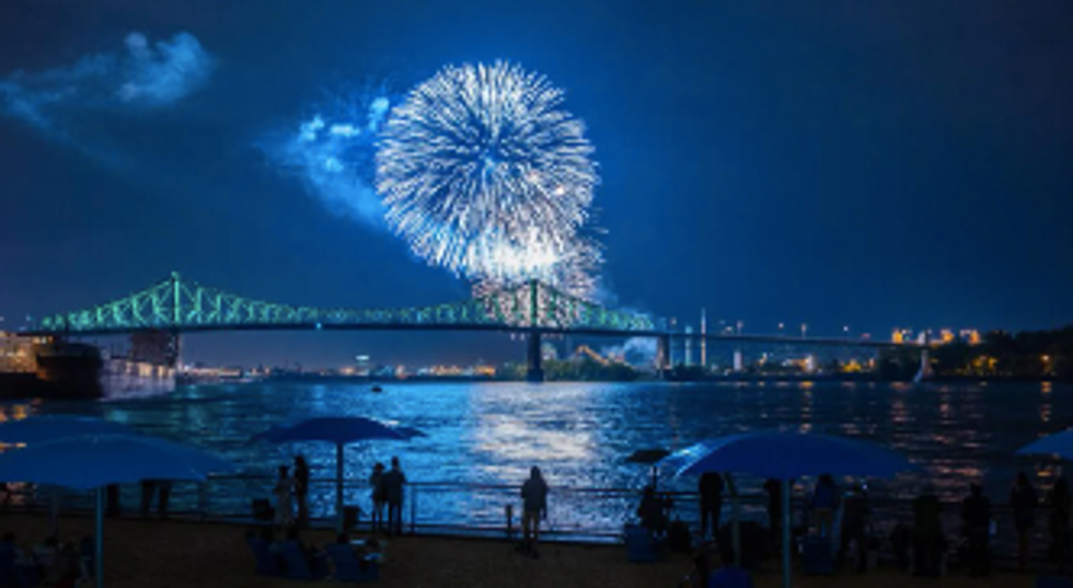 People stand on the Clock Tower Beach watching the fireworks show over the Jacques Cartier Bridge.