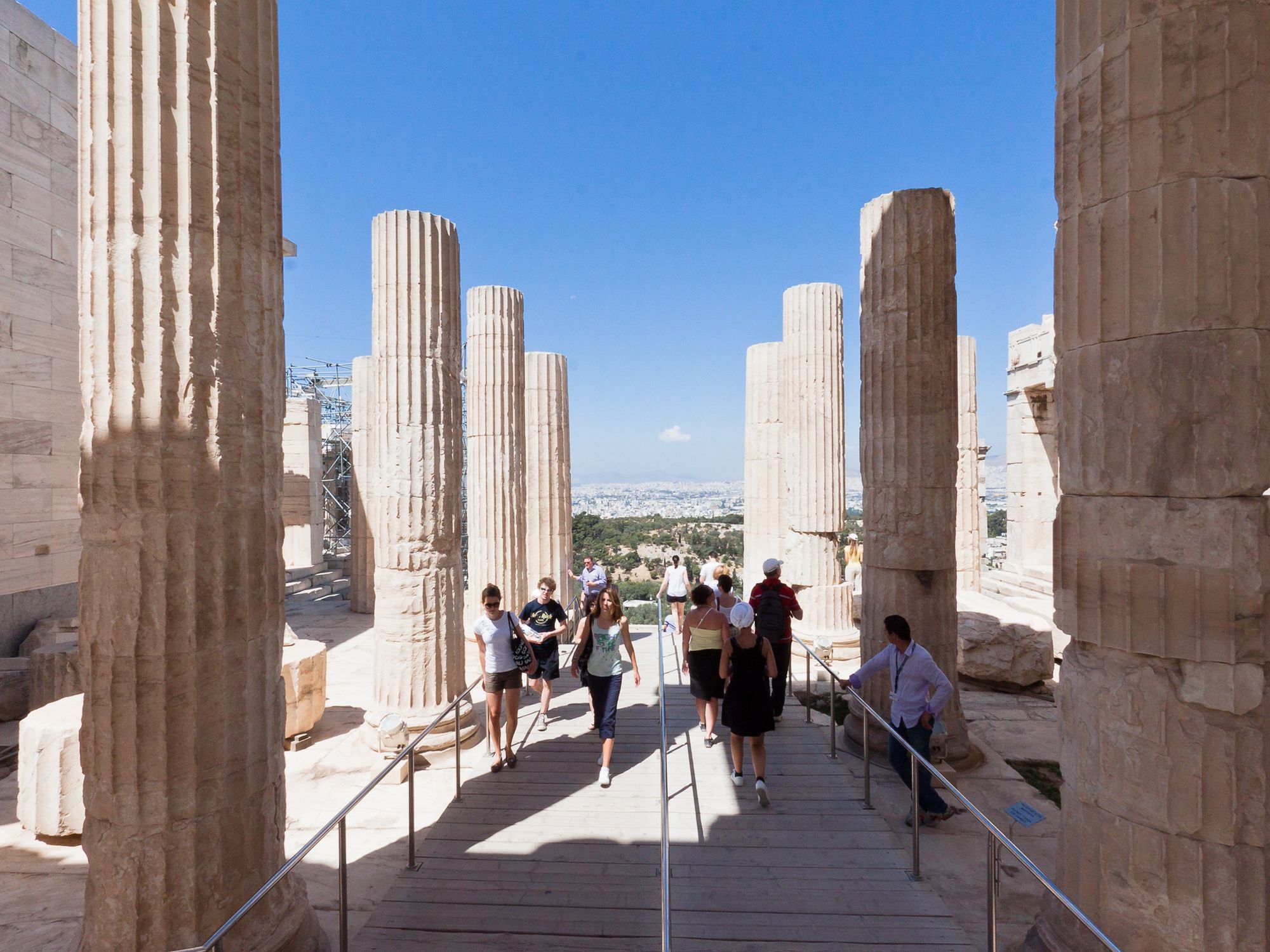 People walk among doric columns at \u200bthe entrance of the Athena Nike temple ruins in the Acropolis of Athens, Greece.