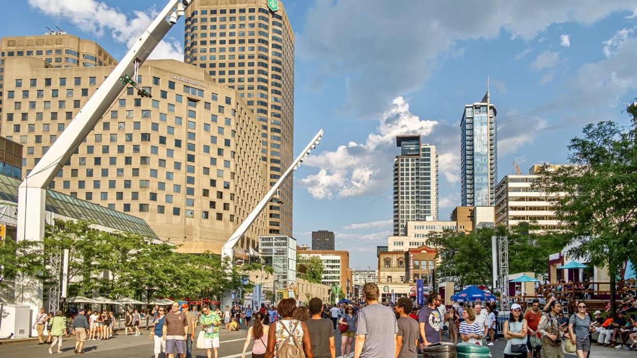 People walking through Quarters des Spectacles during the summertime with the Montreal skyline in the background.