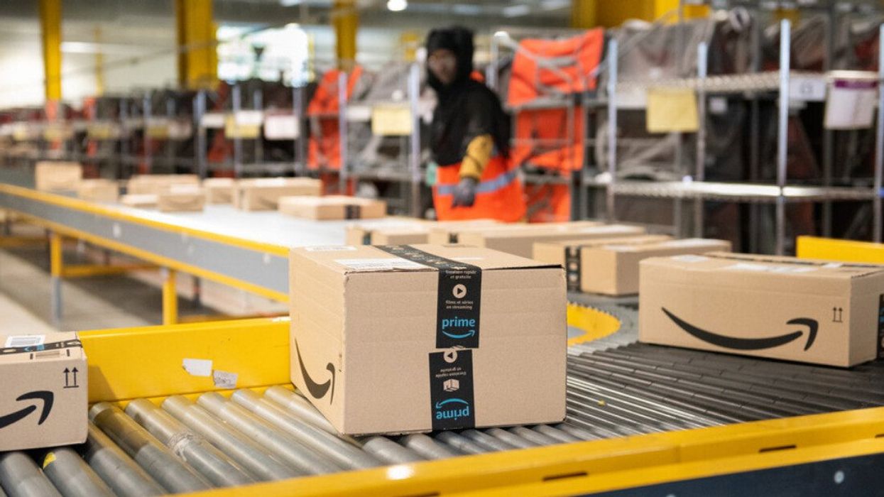 Prime boxes on a conveyor belt moving toward an Amazon employee.