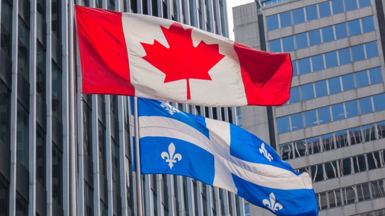 Quebec and Canada flags fluttering in the wind together in the downtown area of Montreal.