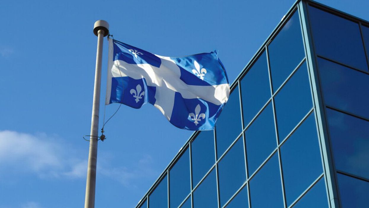 Quebec flag fluttering in the wind in front of a blue glass building .