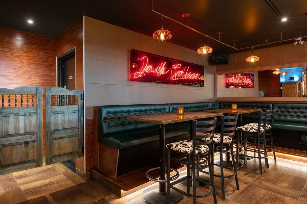 Saloon doors, cow print chairs, booths and a neon sign that reads 'Jack Saloon.'