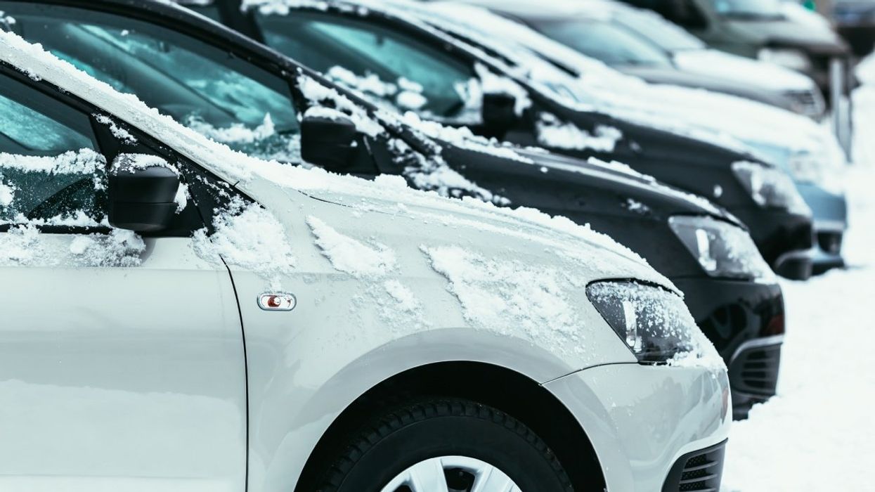 Several sedan cars parked in a parking lot with snow covering its exterior.