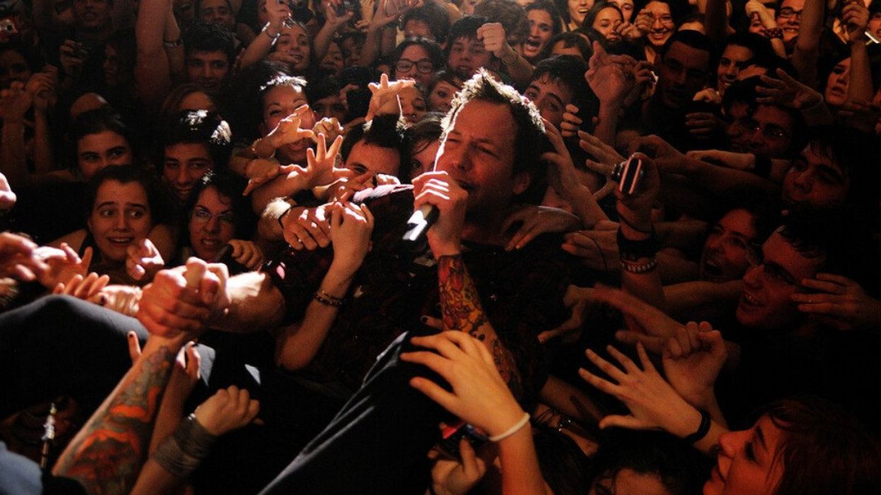 Simple Plan singer Pierre Bouvier holds a microphone while surrounded by fans.