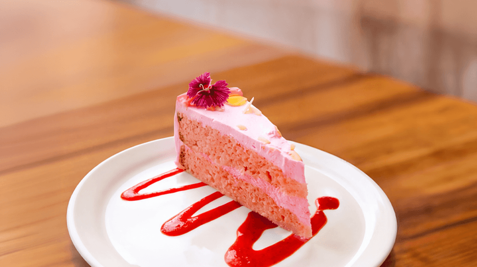 Slice of pink cake with berry sauce on a white plate.