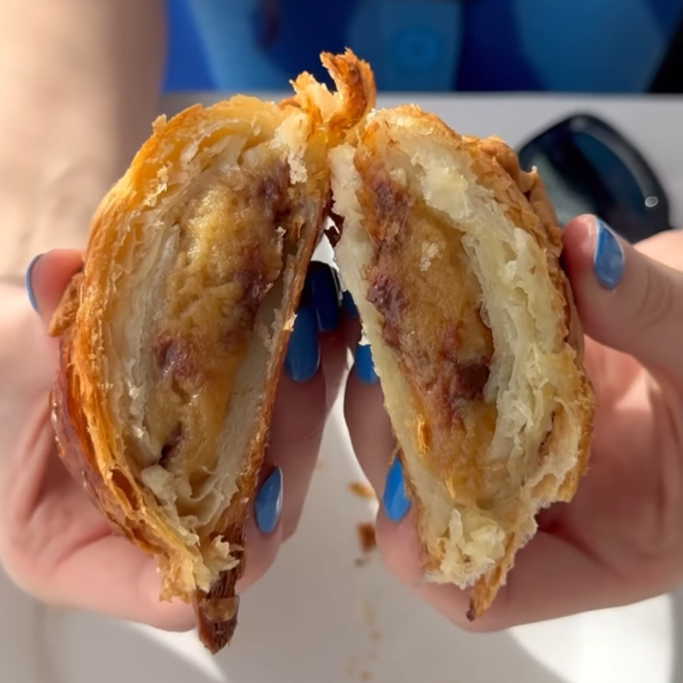 Some holds two halves of a croissant filled with cookie dough.