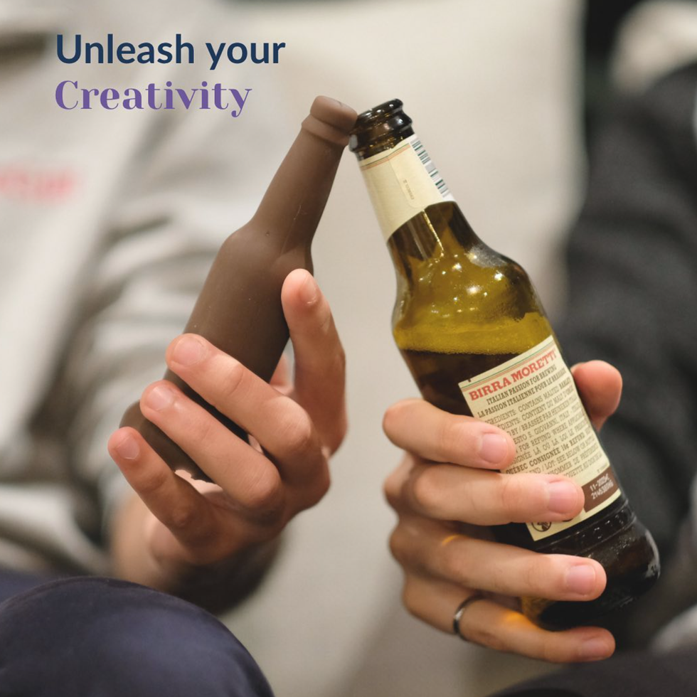 Someone clinks a bottle-shaped brown dildo with a real beer bottle.