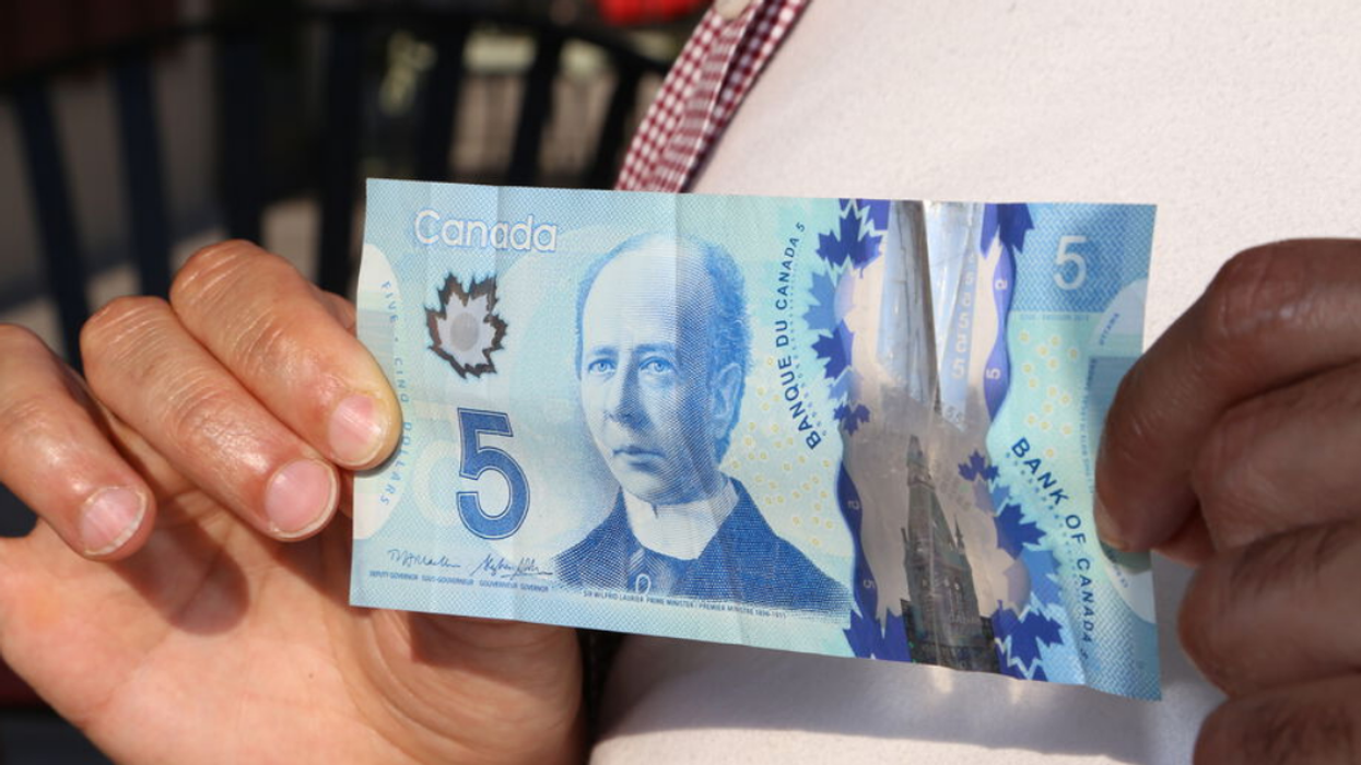 Someone holds a Canadian $5 banknote featuring a portrait of Sir Wilfred Laurier.
