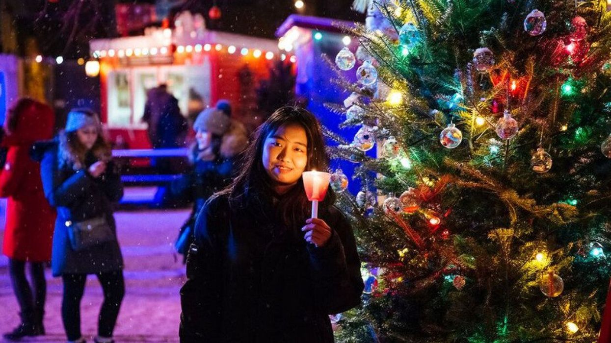 Someone holds a candle by a Christmas tree at Festival Noël dans le Parc.