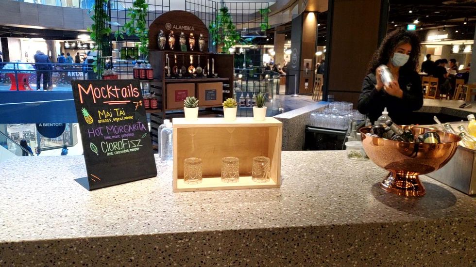 Someone holds a cocktail shaker at the Time Out Montreal mocktail bar, while gamers play on an arcade machine in the background.