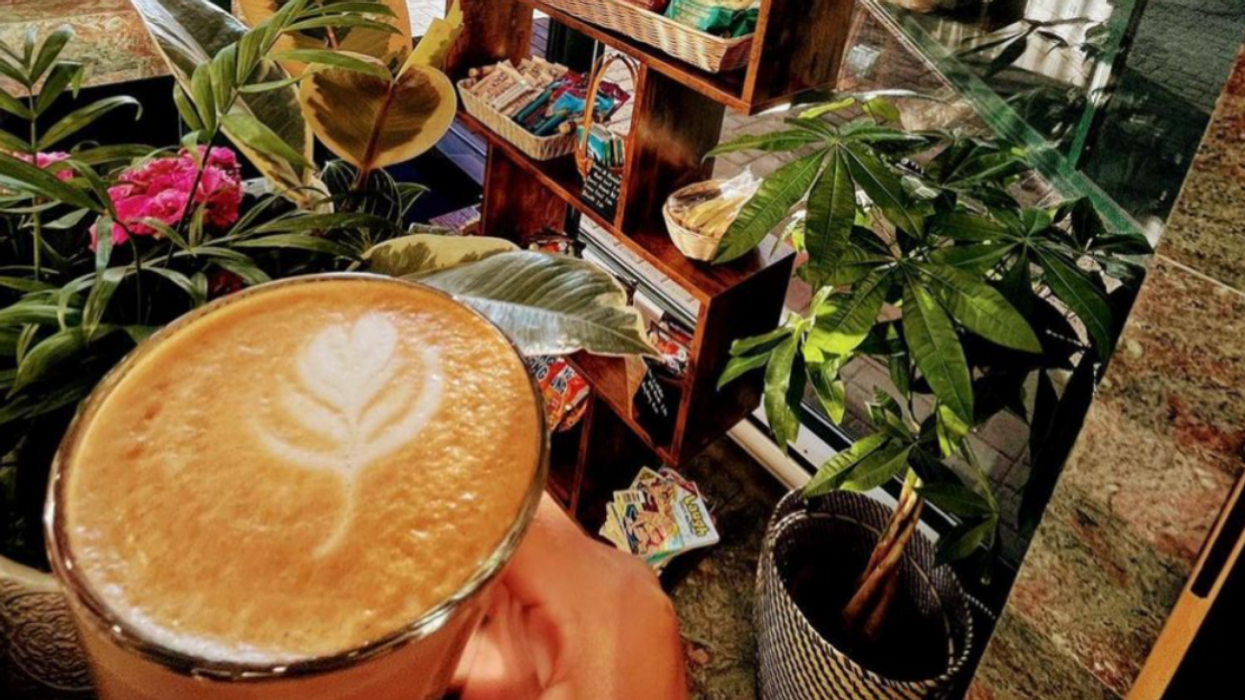 Someone holds a latte in front of a display of products, plants and magazines at Café Le Trooper in Brossard.