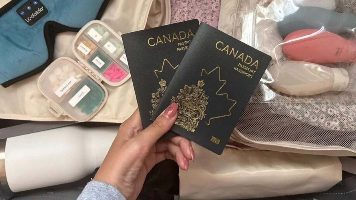Someone holds two Canadian passports above bags in the process of being packed.