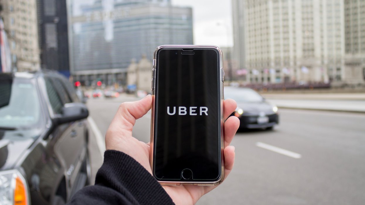 Someone holds up a phone with Uber app loading and busy city street in the background.