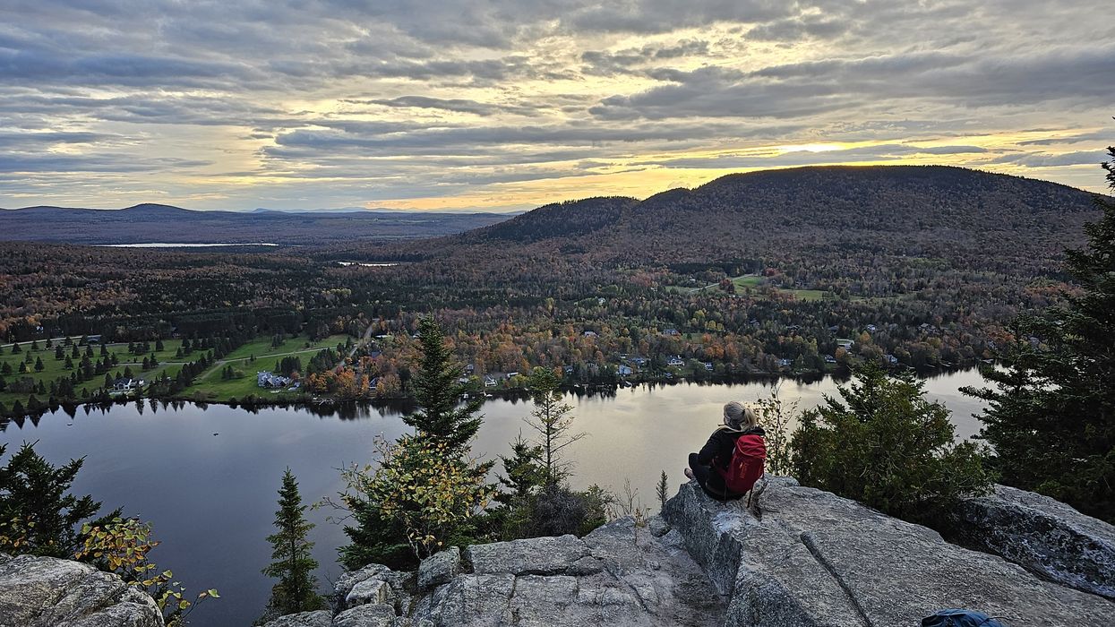 Someone looks out over a river and fall foliage from Mount Pinnacle in Quebec.