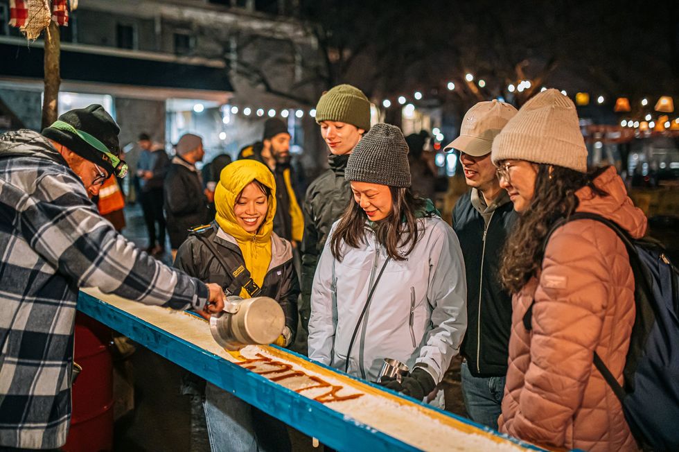 Someone pours maple taffy that spells out "Alice" on ice for a group.
