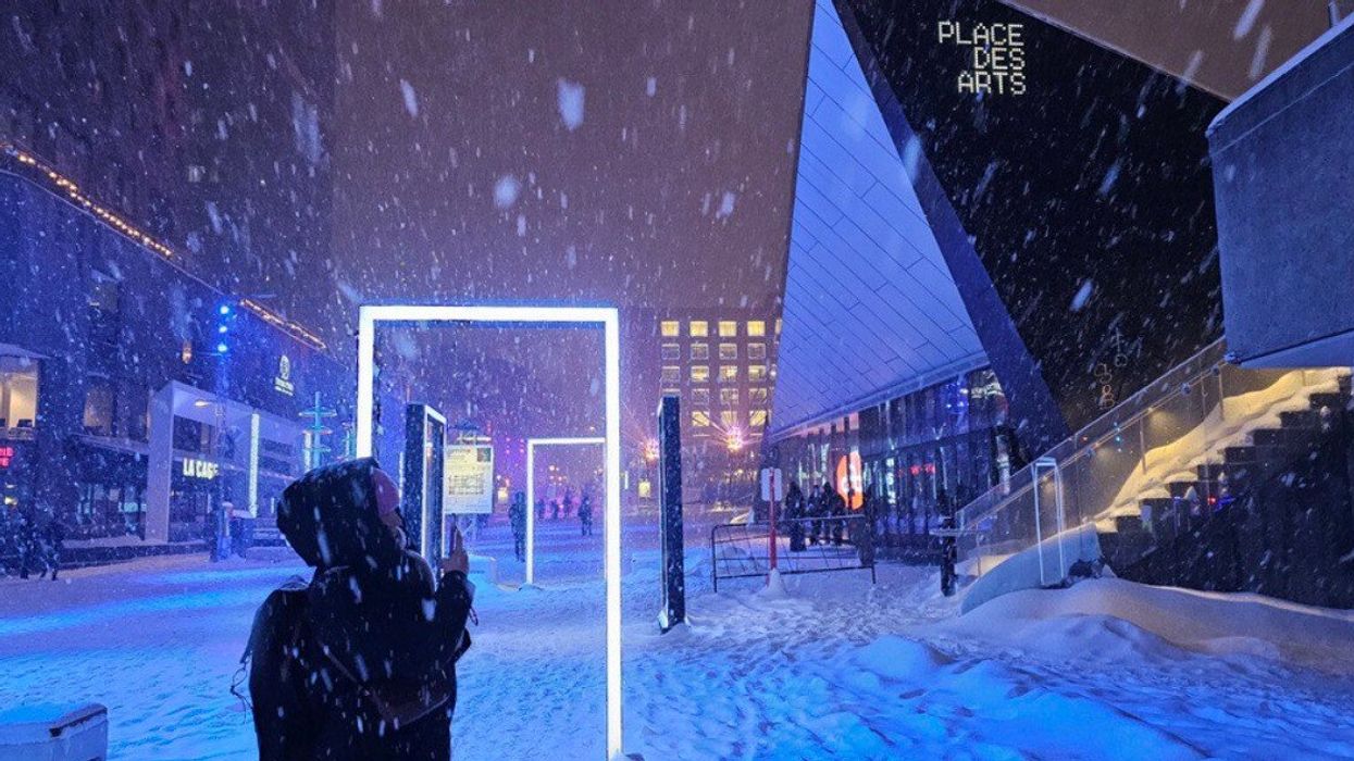 Someone stands by a glowing doorway art installation in Place des Arts during a snow storm.