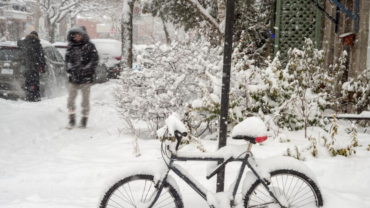 Someone walks on a Montreal sidewalk covered in snow near a snow-covered bike.