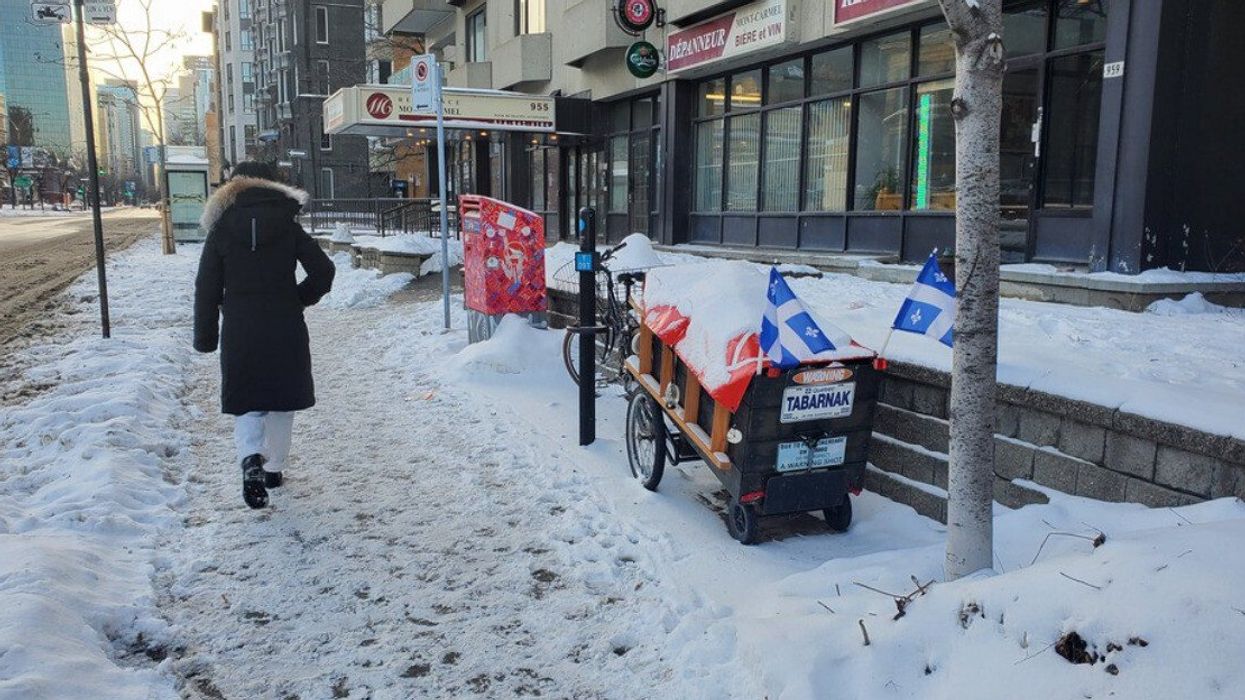 Someone walks on a snowy Montreal sidewalk by a parked bike with Quebec flags.