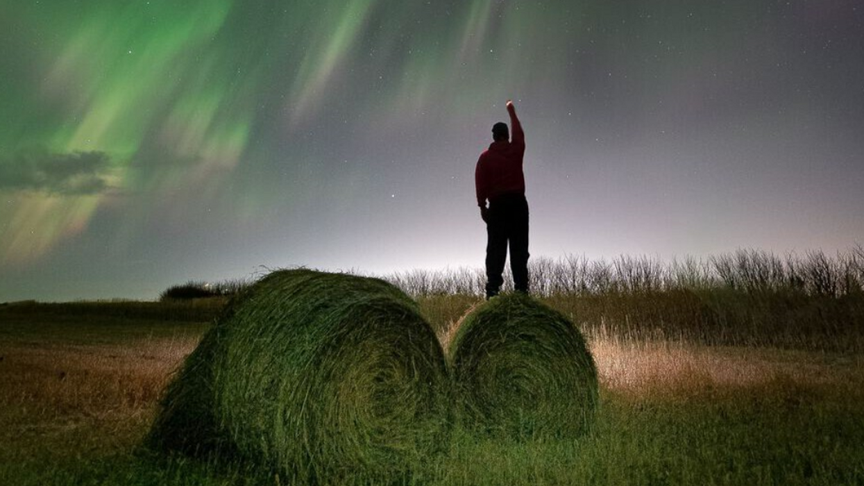 Someone watches the Northern Lights from atop a hay bale in Saskatchewan.