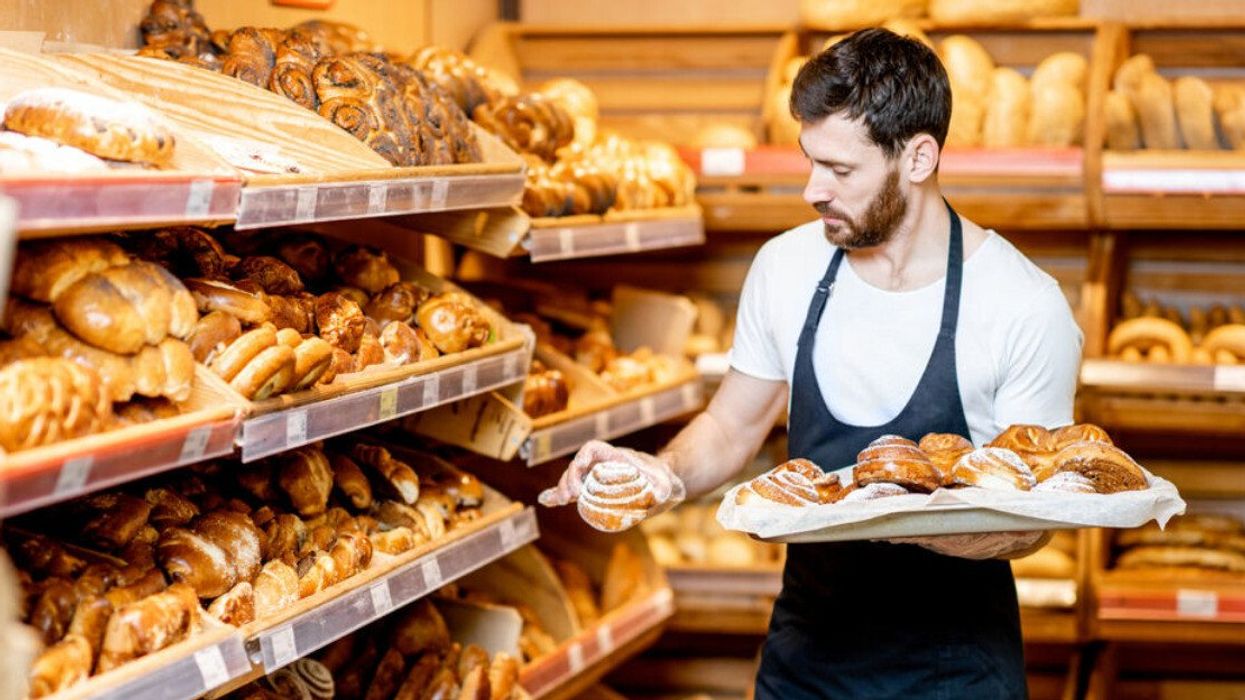 Someone wearing an apron puts baked goods on shelves in a grocery store.