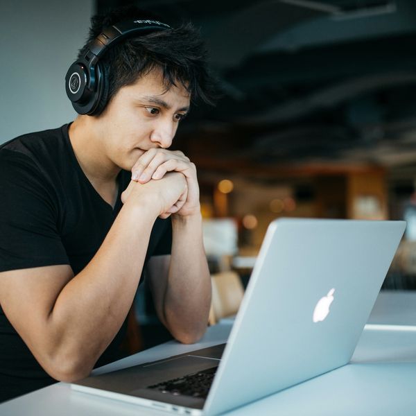Someone wearing headphones sits on chair in front of a MacBook.