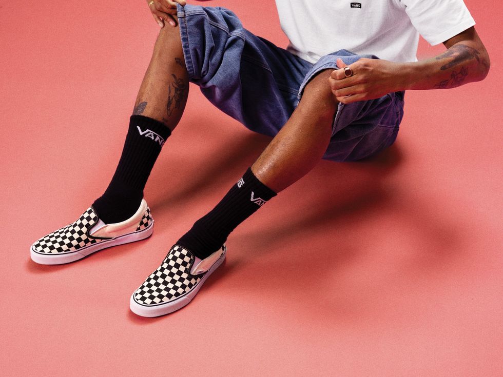 Someone wears checkered Vans slip-ons with long black socks.