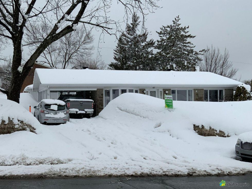 Street-facing fa\u00e7ade of a bungalow in L\u00e9vis, Quebec, with a large pile of snow in front.