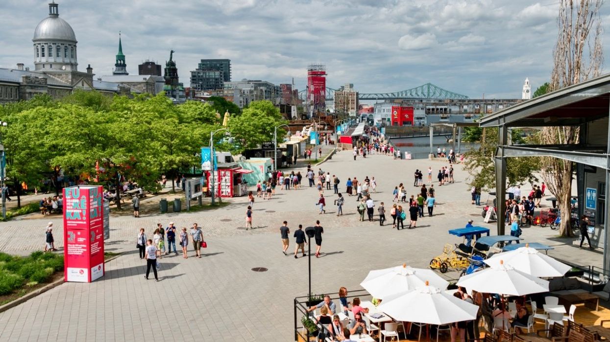 Summer attractions and shops at Montreal's Old Port with people walking the promenade and eating on terraces with the Jacques-Cartier bridge in the background