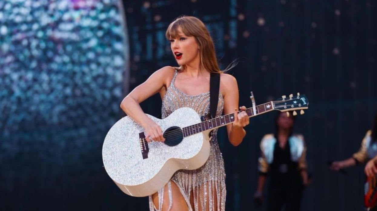 Taylor Swift onstage during her Eras Tour wearing a silver dress all while playing her silver guitar.