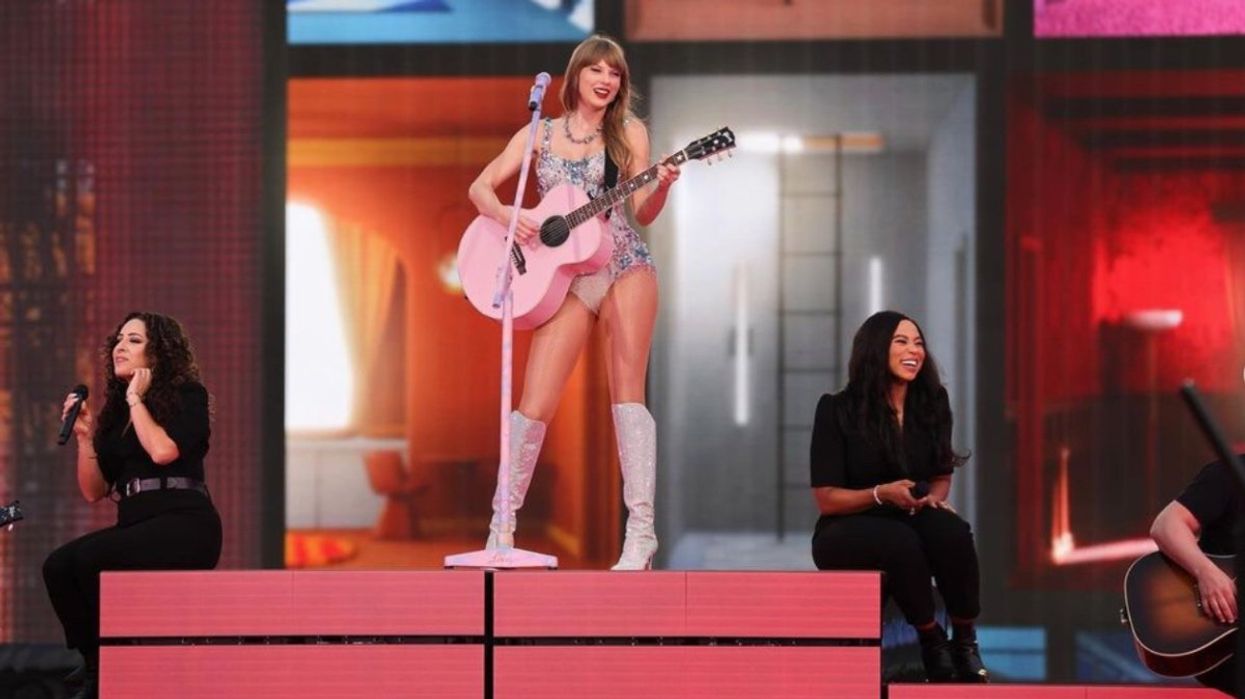 Taylor Swift performing on stage with her guitar and backup singers during her Eras Tour.