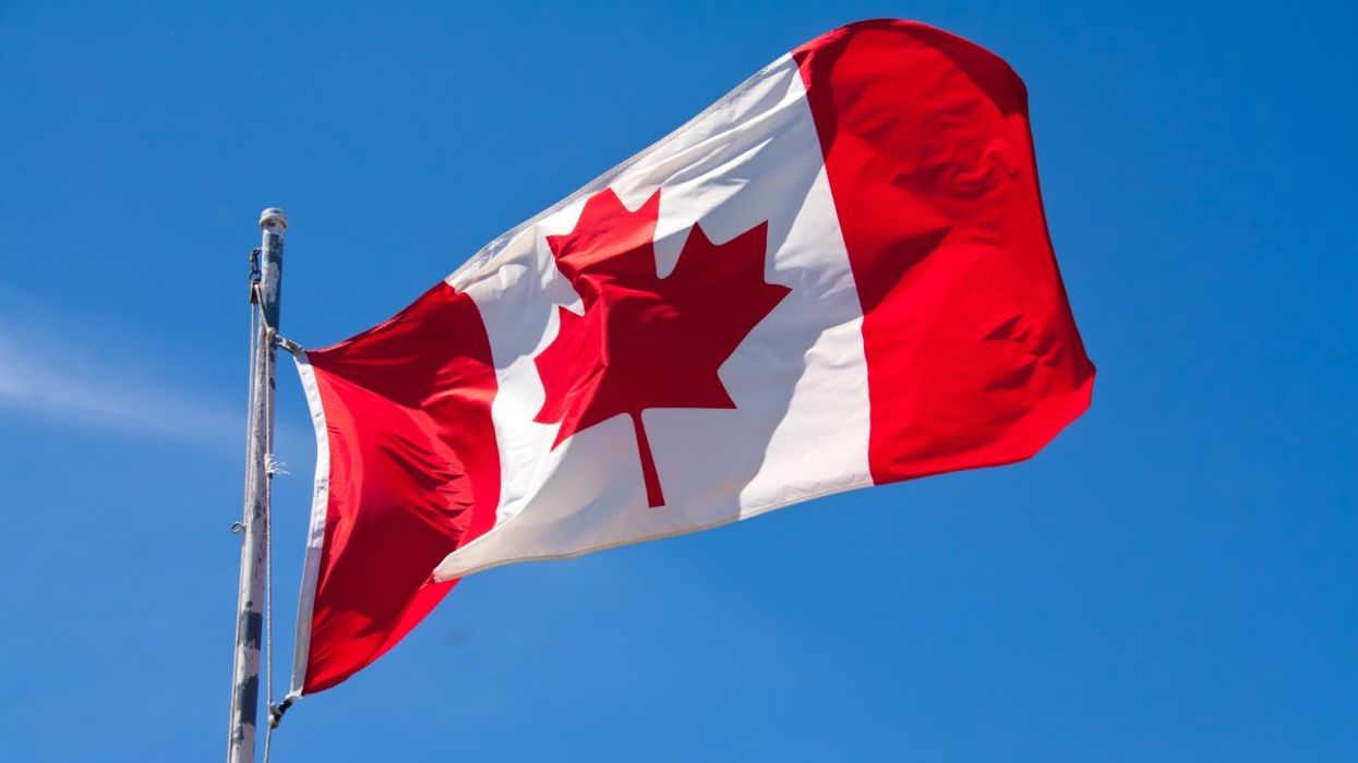 The Canadian flag attached to a flag pole waving with a clear blue sky backdrop.